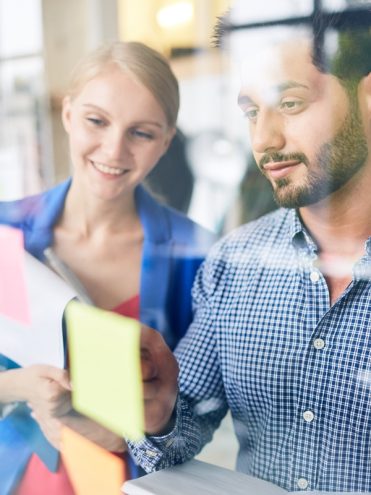 Two young managers discussing one of reminders on notepaper at the beginning of working day